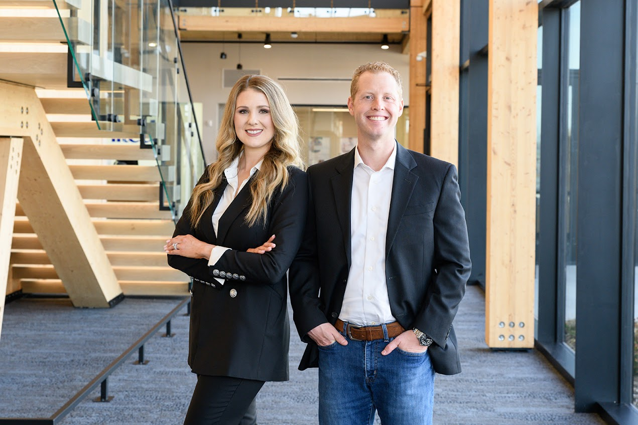 Two professionals in business attire standing confidently inside an office building.